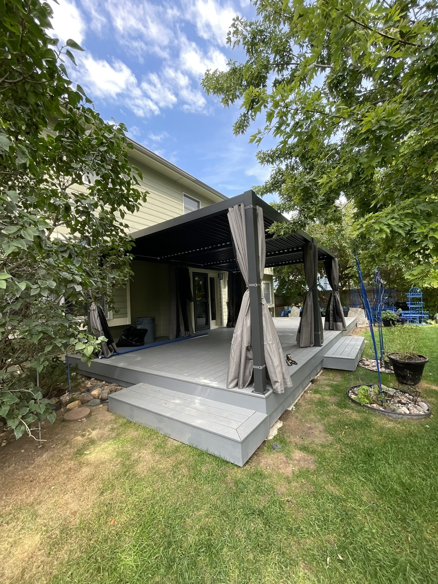 Ground-level deck with a louvered pergola surrounded by trees