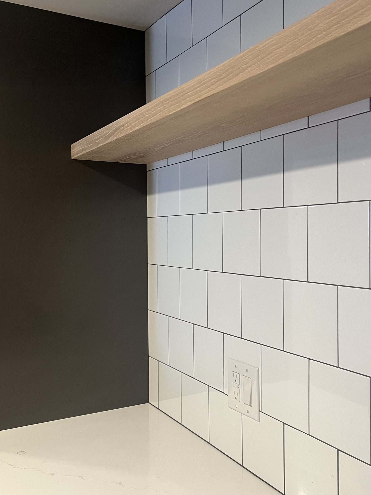 Wood floating shelf over a white tile backsplash