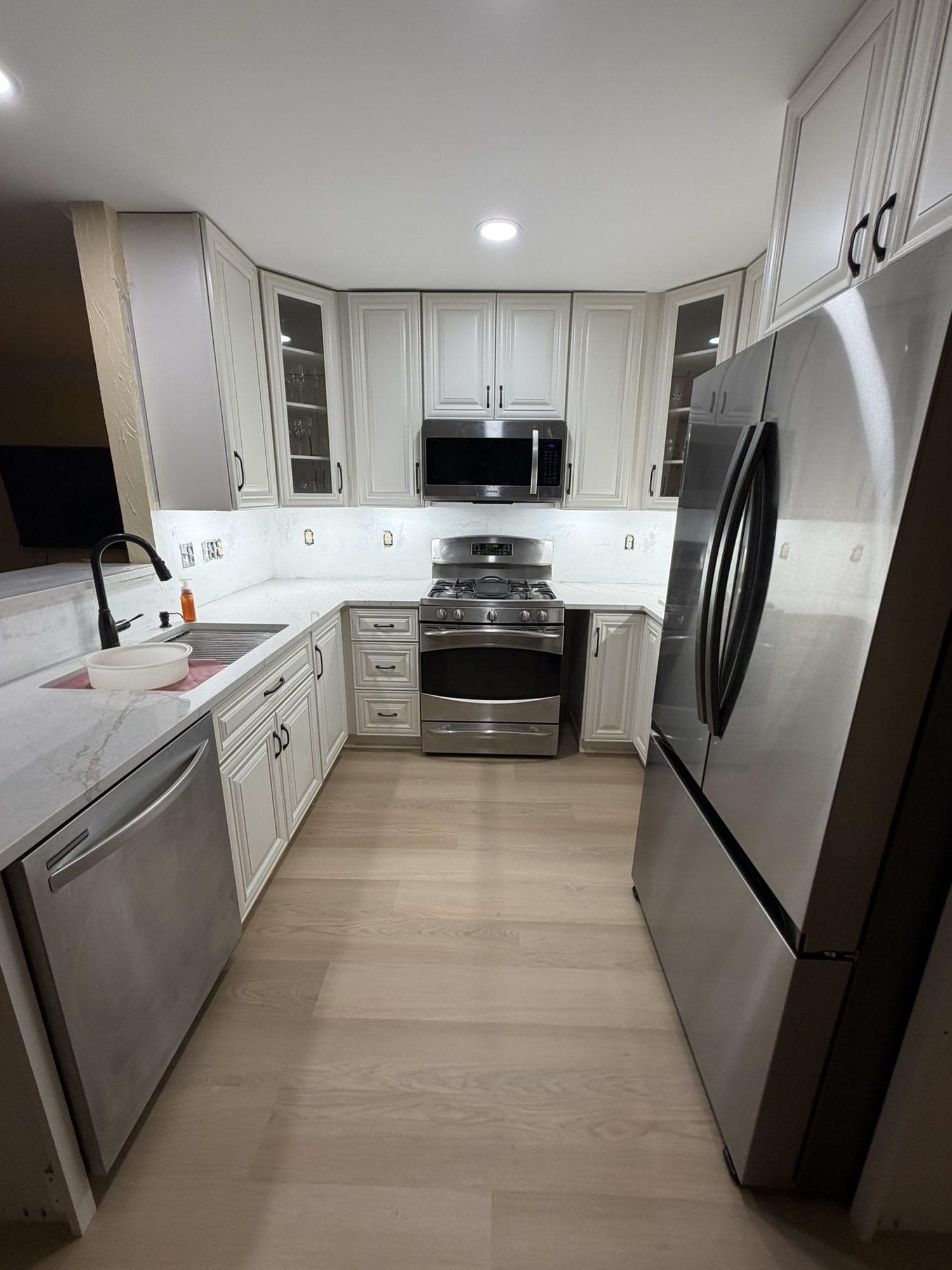 Galley kitchen with cream cabinets, stainless appliances and wide-plank flooring