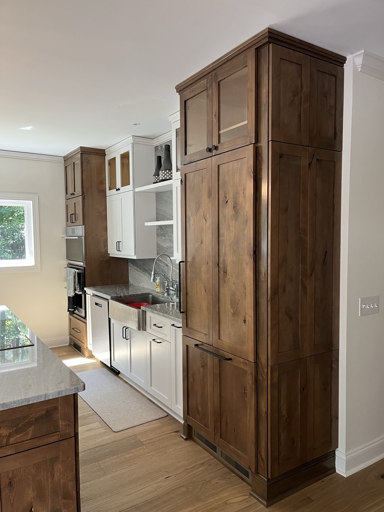 Full-height knotty alder pantry cabinet beside a run of white kitchen cabinets